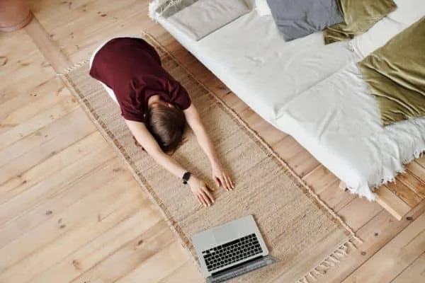 A person practicing yoga at home with a laptop set up for a live online class