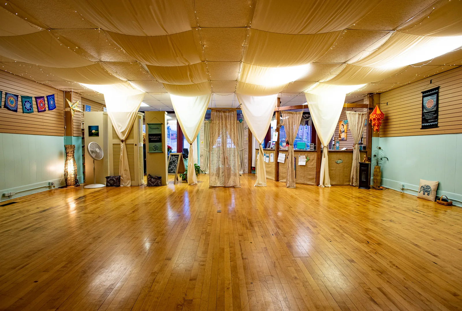 The light-filled main practice room at Grace Yoga and Pilates in Daleville, Virginia, with draped fabric, fairy lights, and warm wood floors